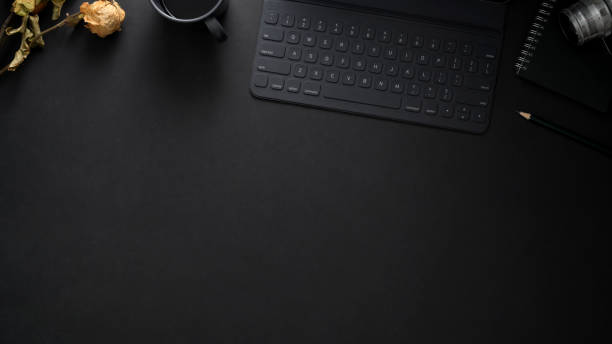 istock Top view of  workplace with wireless keyboard, copy space, camera and dry roses on black table 1206182178