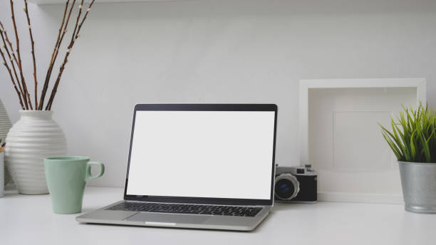 istock Cropped shot of workplace with blank screen laptop, frame, decorations and camera on white desk 1206182345