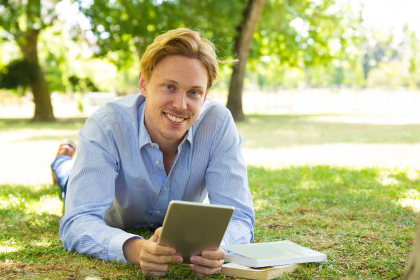 istock Cheerful young man lying on ground with tablet 1206182785