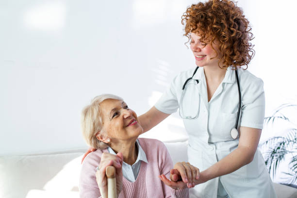 Happy patient is holding caregiver for a hand while spending time together. Elderly woman in nursing home and nurse. Aged elegant woman at nursing home Happy patient is holding caregiver for a hand while spending time together. Elderly woman in nursing home and nurse. Aged elegant woman at nursing home common room stock pictures, royalty-free photos & images