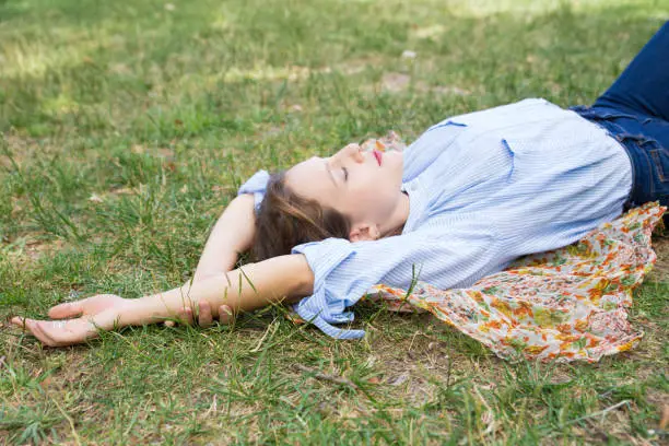 Relaxed young woman lying on headkerchief on ground in park. Beautiful lady relaxing outdoors. Leisure, relaxation concept