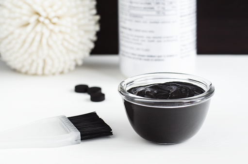 DIY activated charcoal peel off mask in the small glass bowl. Homemade beauty treatment. Top view, copy space.