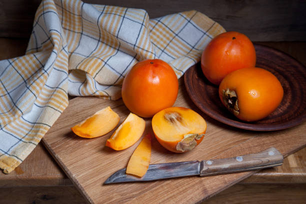 istock Whole ripe persimmon and sliced fruit on a wooden background. 1206197546