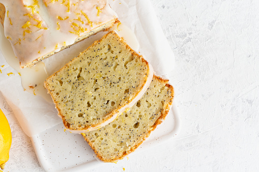 Lemon bread coated with sugar sweet icing and sprinkled with lemon peel. Slice of cake with citrus, poppy, traditional american cuisine. Copy space, top view