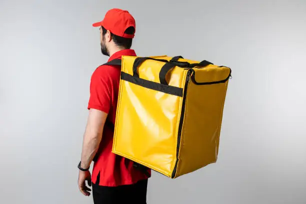 Photo of Side view of courier with thermo backpack isolated on grey