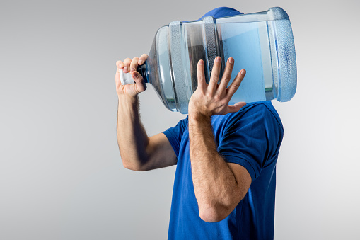 Side view of courier carrying on shoulder bottle of water isolated on grey