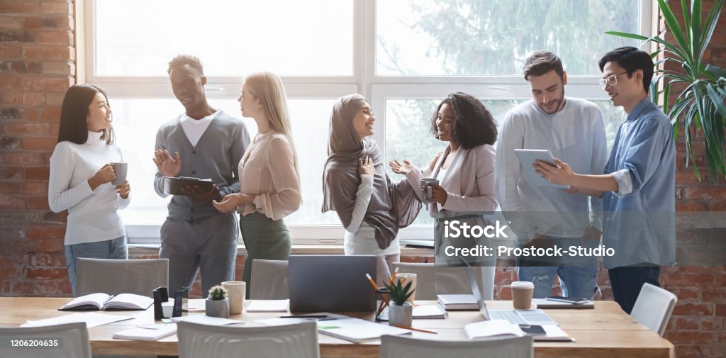 Multiracial young happy people sharing ideas while coffe break Group of happy multiracial young people sharing ideas and having conversation while coffe break at business meeting at office, panorama Multiracial Group Stock Photo