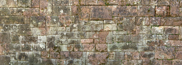 Panorama - Old, heavily weathered and partly mossy wall made of red sandstone with different sized rectangular stones