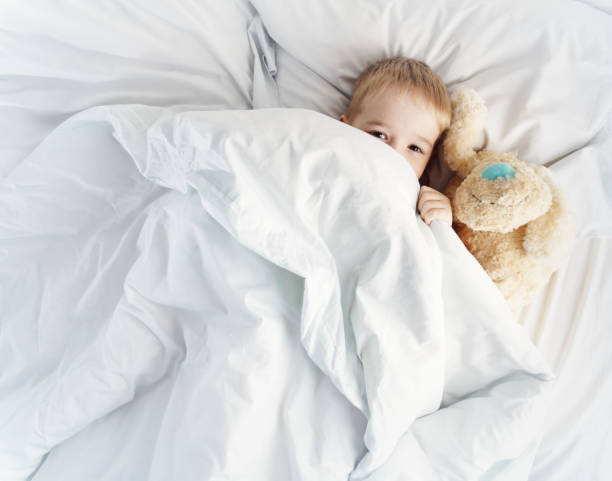 istock Sleepy boy lying in bed with white beddings 1206208158