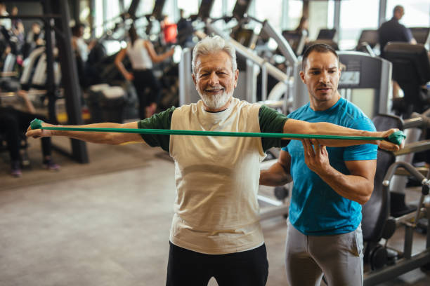 istock Male instructor assisting senior man exercising with resistance band at gym 1206214950