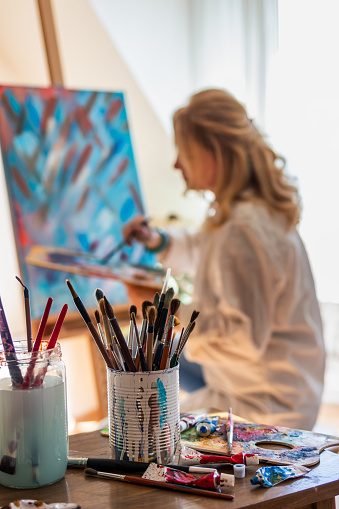 Selective focus on paintbrushes, palette and colors. Woman in art studio