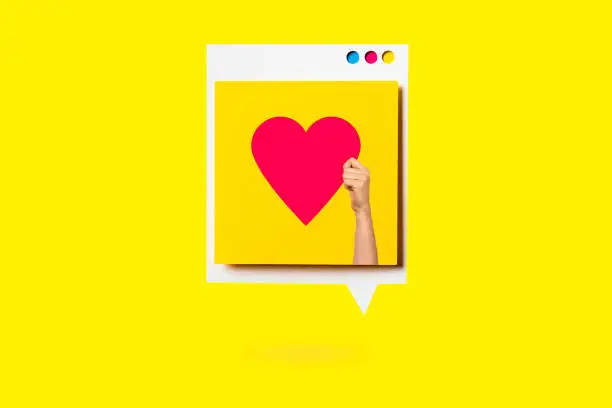 Photo of Paper cutout of red heart symbol on a white speech bubble on yellow background. Concept of social media and digital marketing.