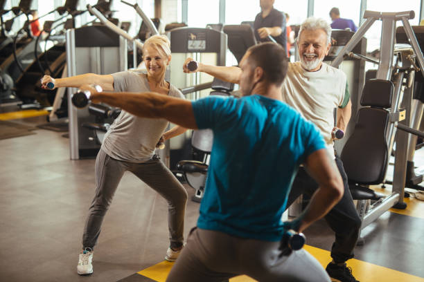 istock Senior couple exercising with personal trainer using dumbbells at the gym 1206219487