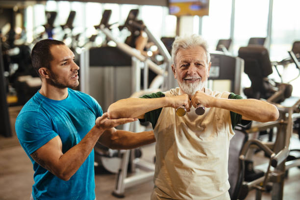 istock Senior man exercising with personal trainer using dumbbells at the gym 1206219548
