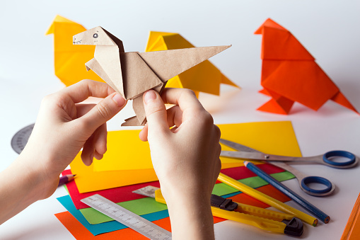 girl makes origami dinosaur of colored paper. paper, ruler, pencils, knife. interesting hobby\