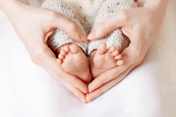 母親の手に赤ちゃんの足。女性のハート型の手のクローズアップに小さな新生児の足。ママと彼女の子供。ハッピーファミリーのコンセプト。マタニティの美しい概念的イメージ - 足 ストックフォトと画像