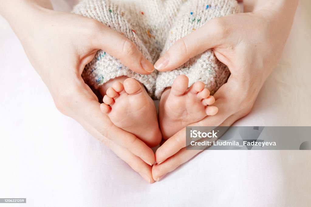 Baby feet in mother hands. Tiny Newborn Baby's feet on female Heart Shaped hands closeup. Mom and her Child. Happy Family concept. Beautiful conceptual image of Maternity Baby - Human Age Stock Photo