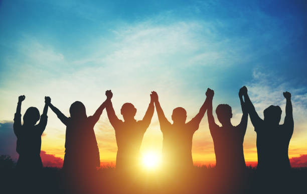 silhouette del team aziendale di gruppo che fa mani alte sopra la testa nel cielo al tramonto - vittoria foto e immagini stock