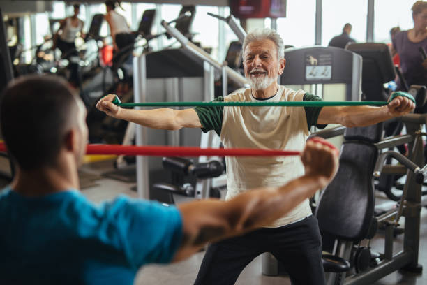 istock Senior man exercising with personal trainer using resistance band at the gym 1206236480