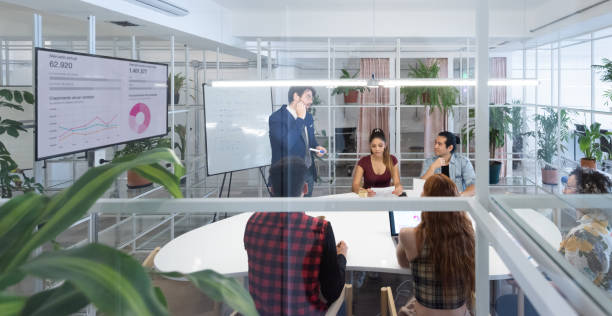 Presentation in multi ethnic business team meeting, seen from outside through windows
