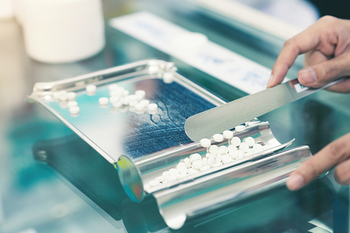 Medicine tablets on counting tray with counting spatula at pharmacy.
