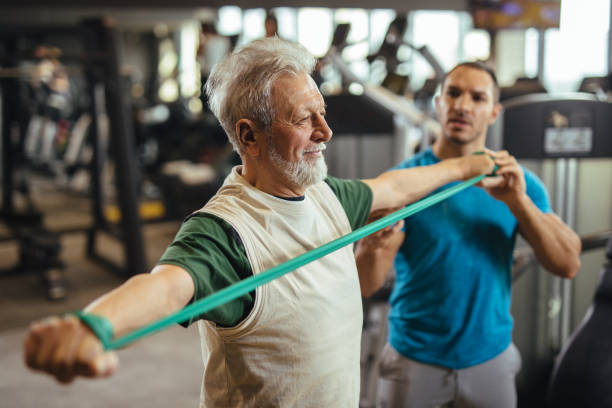 istock Senior man exercising with personal trainer using resistance band at the gym 1206239614