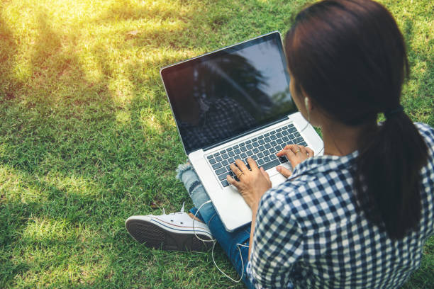 istock woman sit to use computer laptop on green grass at public park 1206240712