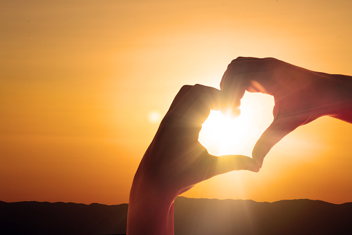 Corazón en forma de mano contra la puesta del sol photo