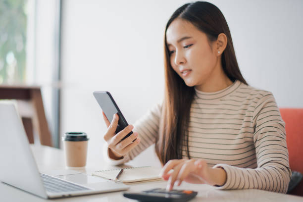 istock Young woman using a calculator and other hand using phone to chat with customer and have notebook on the table at cafe or co working space which smiling and felling happy. co working space concept. 1206244899