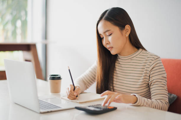 istock Young Asian woman using a calculator and other hand using pencil take a note in the book and have notebook on the table at cafe or co working space. co working space concept. 1206246231