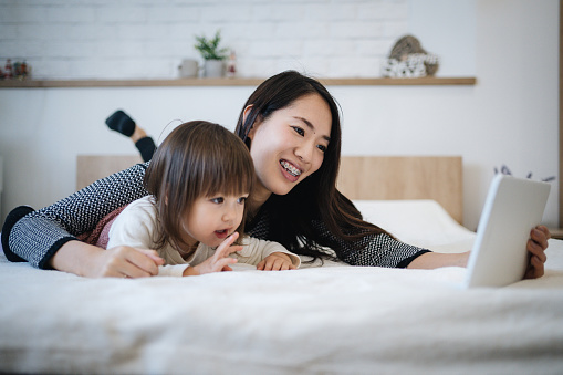 Young mother watching cartoons on tablet with her daughter in bedroom
