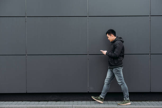 istock side view of young asian man chatting on smartphone while walking along wall 1206250635