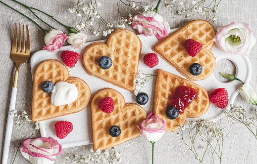 Homemade Belgian heart waffles with strawberry sauce and berries, pink flowers, spring, Woman day, morning concept, Valentine's day