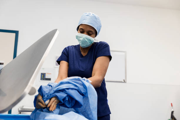 Mature female surgeon taking off surgical gown After a successful surgery, a female surgeon takes off a surgical gown and places it in a waste bin. undressing stock pictures, royalty-free photos & images