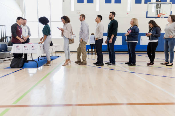 Group of people wait in long line in polling place A long line of people wait to vote in poling place. A few of the people pass the time by using their smartphones. democratic party usa photos stock pictures, royalty-free photos & images