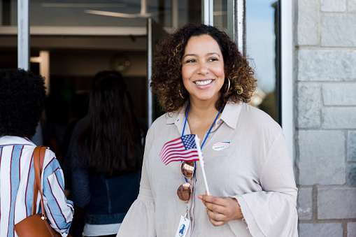 Proud mid adult woman holds a US flag after voting on election day.
