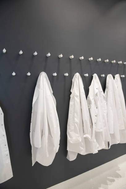 Medical Protective Clothing Medical protective clothing hanging in a hallway. White lab coats in a row in preparation for a pandemic coat hook photos stock pictures, royalty-free photos & images