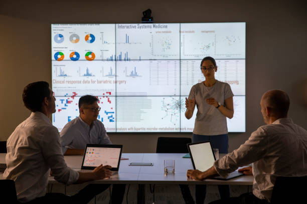 Female Leads the Meeting on Drug Development Meeting in front of a large information device about universal detection of genes in a specific biological sample. data mining stock pictures, royalty-free photos & images