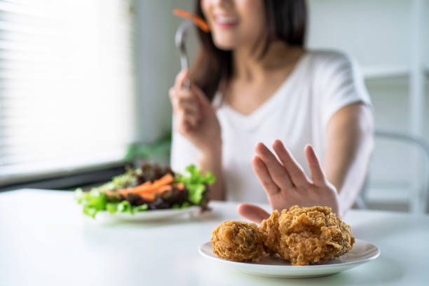 mulher em dieta para um bom conceito de saúde, mulheres jovens usam as mãos para empurrar frango frito e optam por comer vegetais para uma boa saúde. - gordura nutriente - fotografias e filmes do acervo