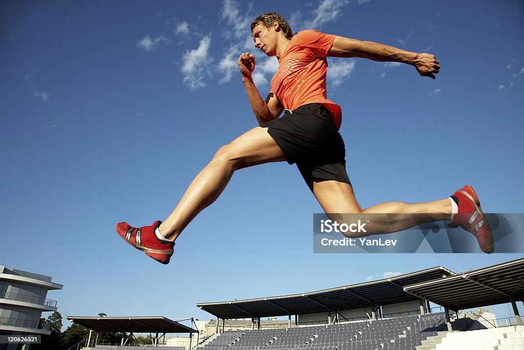 running young muscular athlete is running  at the stadium background of blue sky Activity Stock Photo