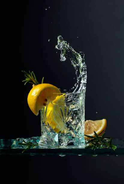 Cocktail gin-tonic with lemon and rosemary on a glass table. Cocktail gin-tonic with lemon and rosemary. Carbonated drink with ice pieces on a glass table. Black background, copy space. gin tonic stock pictures, royalty-free photos & images