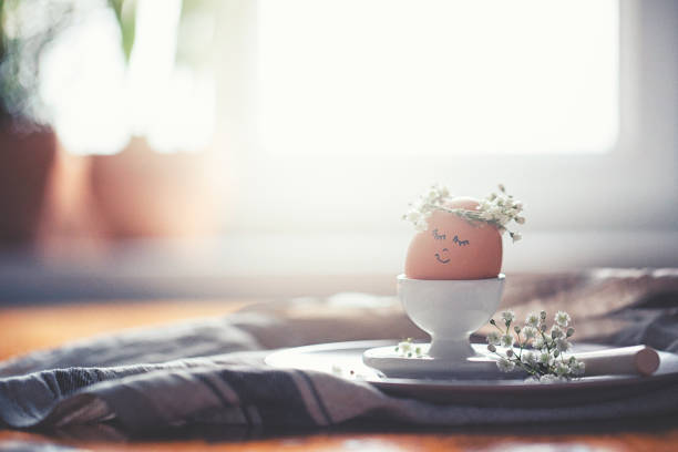Natural easter egg in an eggcup with funny painted face and sweet flower wreath on Easter breakfast