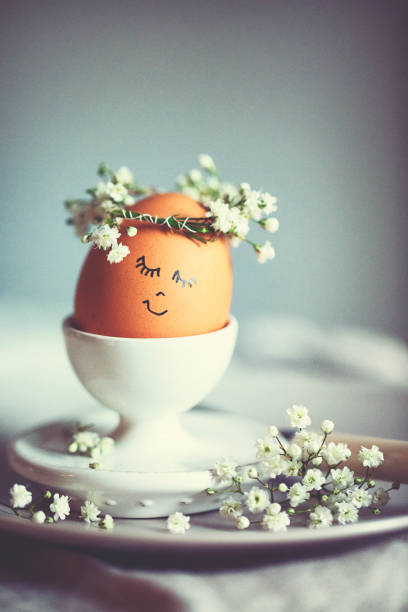Natural easter egg in an eggcup with funny painted face and sweet flower wreath on Easter breakfast