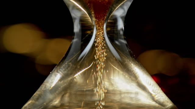 SLO MO LD Golden sand falling through an hourglass