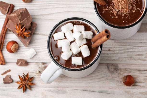 istock Two mugs hot chocolate with cinnamon and marshmallow on wood table decorated with chocolate pieces, almonds, hazelnut and anise top view. 1206284271