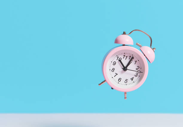 istock Pink alarm clock flies in the air on a blue background. Levitation effect 1206285932