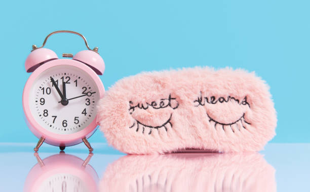 istock Sleep optimization. Pink fluffy mask for sleeping and a pink alarm clock on a light blue background. 1206285949