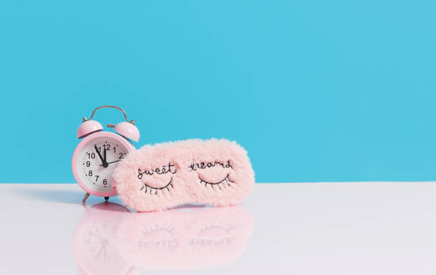 Sleep optimization. Pink fluffy mask for sleeping and a pink alarm clock on a light blue background.