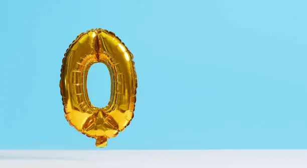 Photo of Golden foil balloon in the shape of numbers on a blue background. Levitation effect