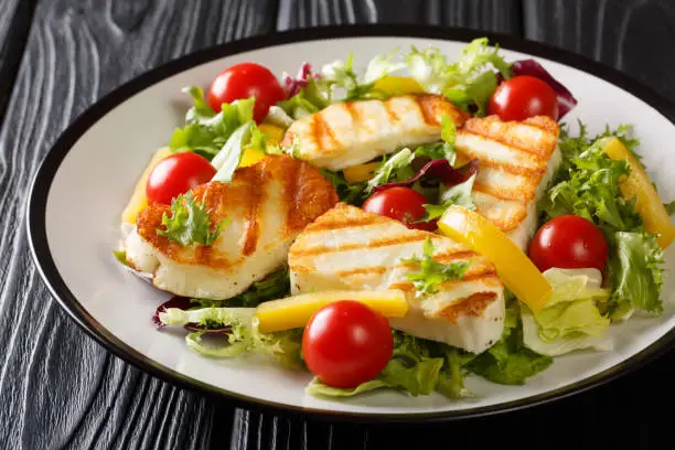 Tasty snack salad Grilled halloumi cheese filed with fresh vegetables close-up on the plate on the table. horizontal